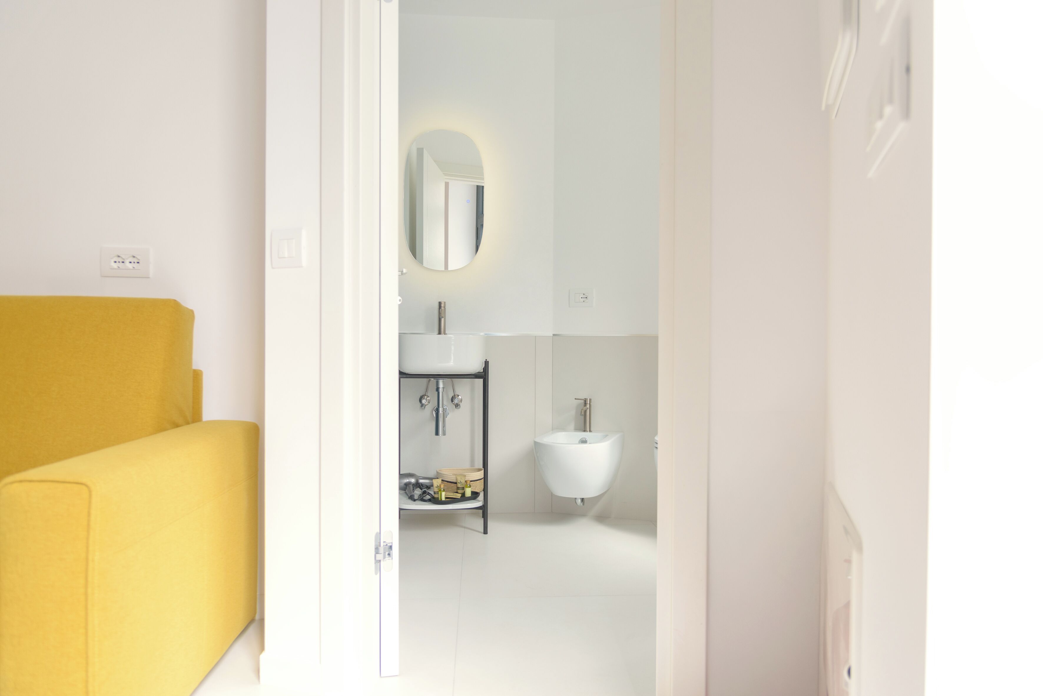 Un baño moderno con un lavamanos blanco, un espejo y una silla amarilla en primer plano.