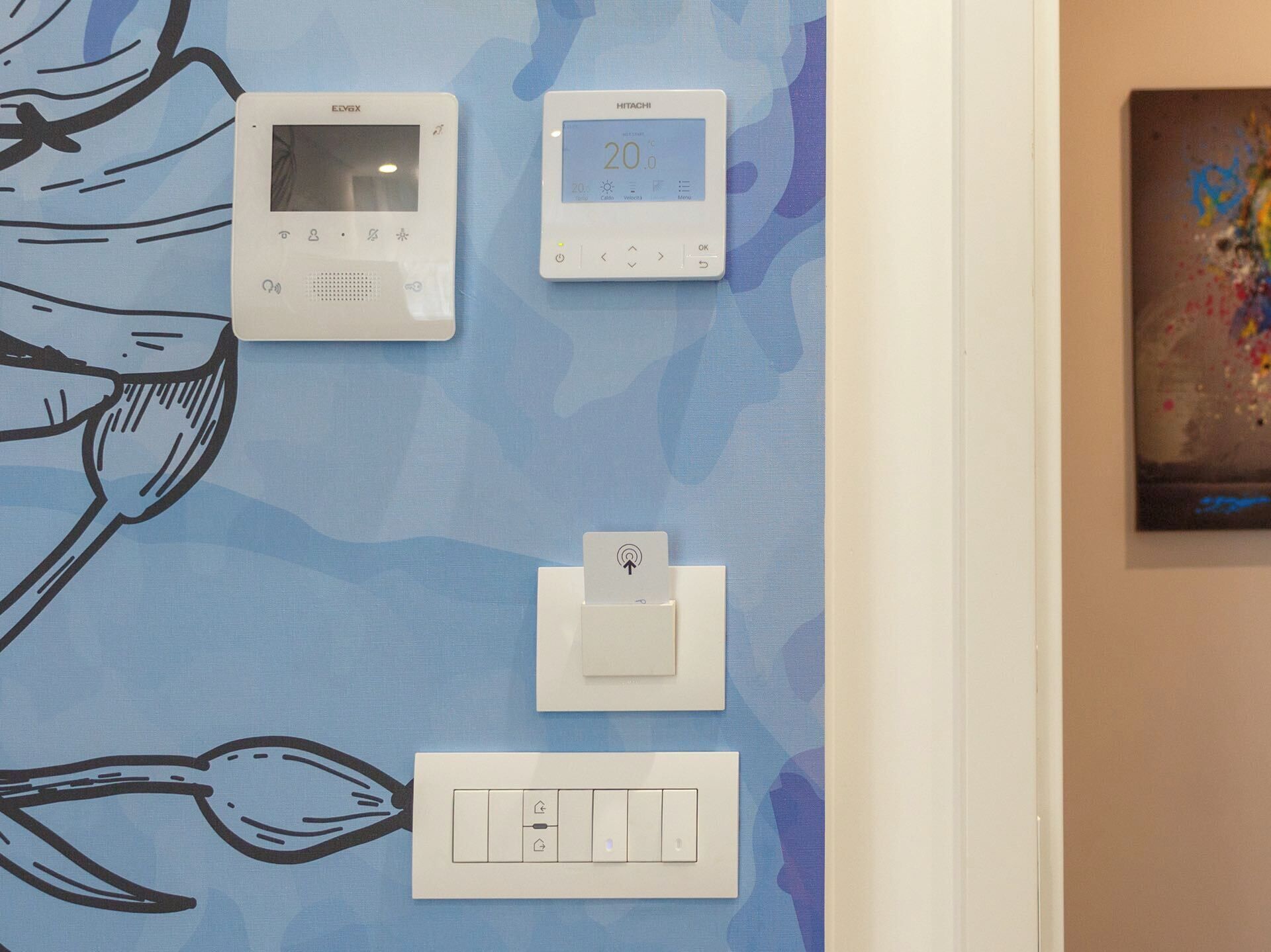 A wall with a thermostat, a control panel, and a light switch.