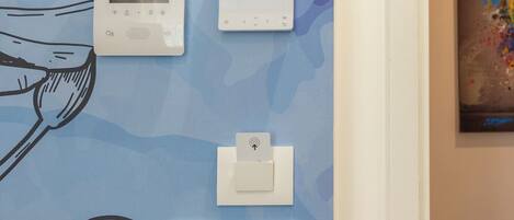 A wall with a thermostat, a control panel, and a light switch.