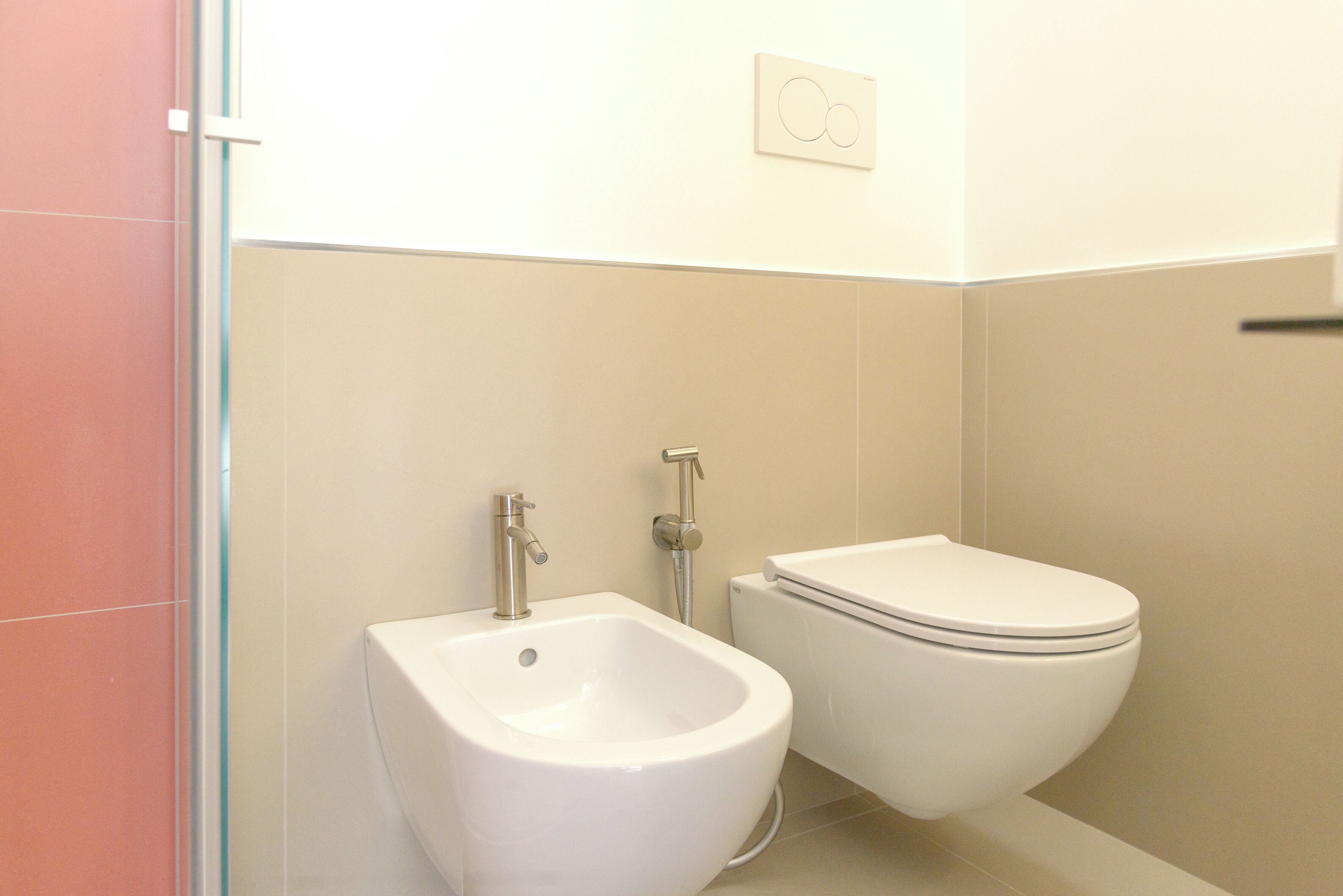 A bathroom with a bidet, toilet, and a wall-mounted light switch.