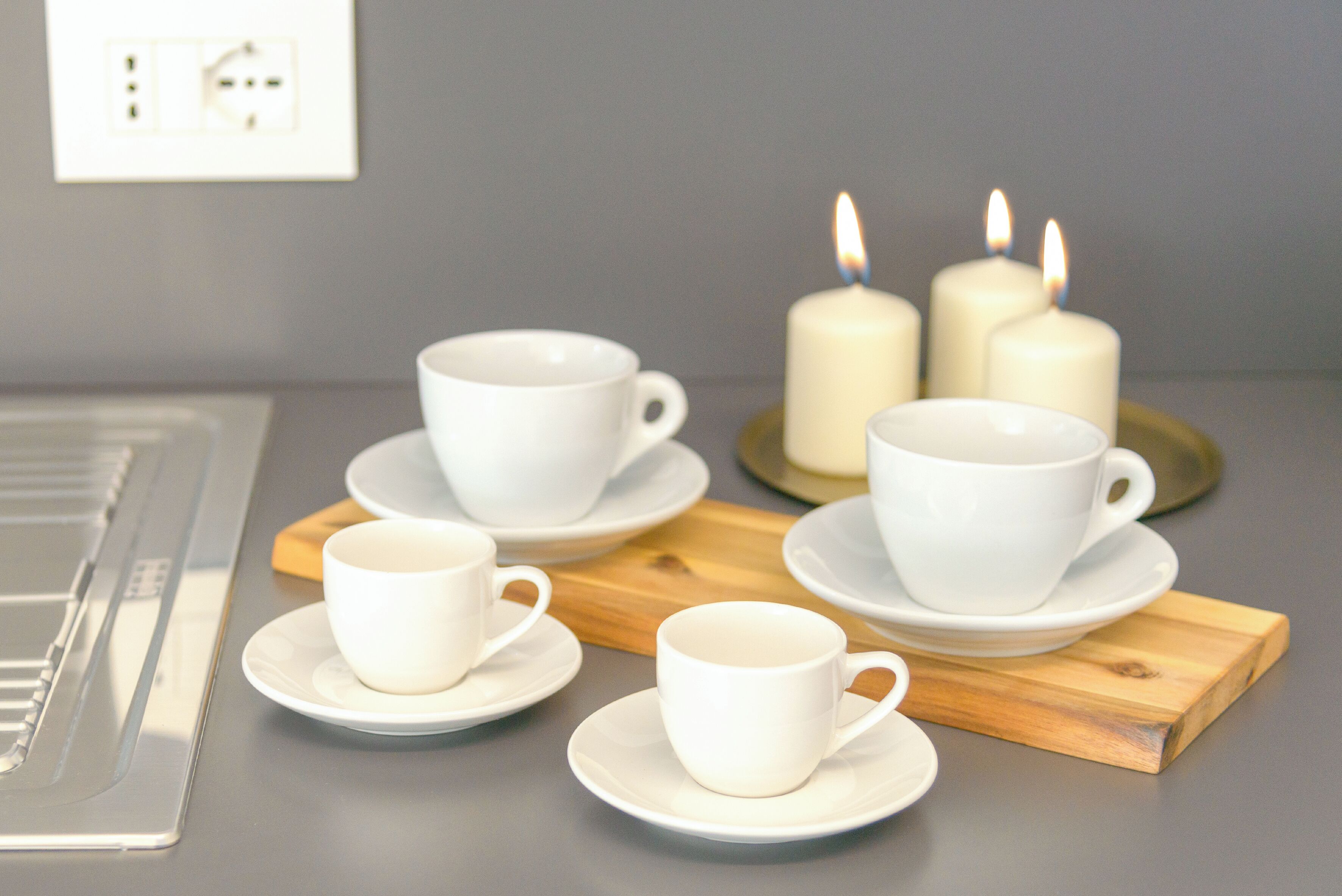 Una mesa con tazas y platillos blancos, velas y una bandeja de madera.