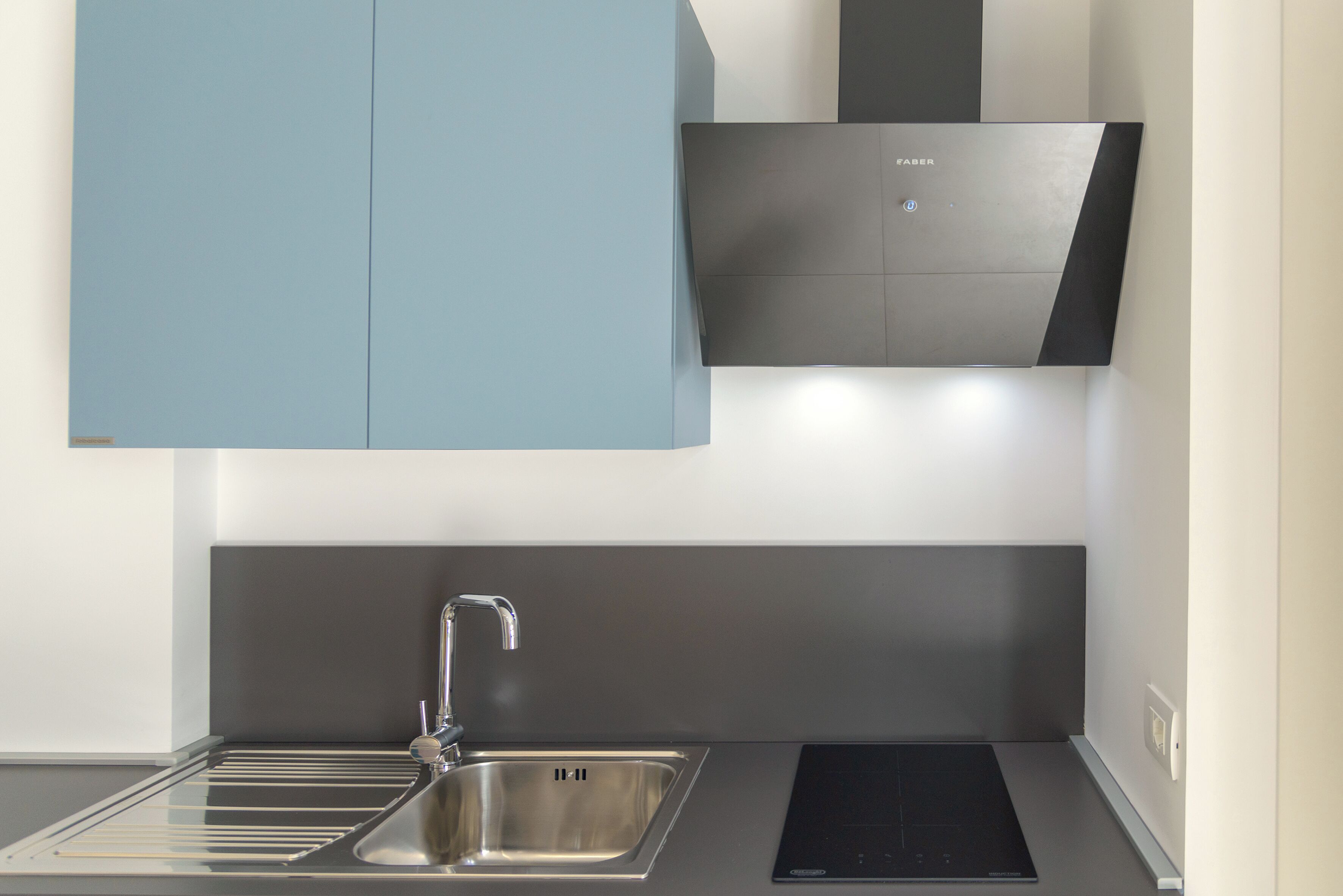 Una cocina moderna con un lavamanos de acero inoxidable, una placa de cocina por inducción negra y un armario azul elegante.