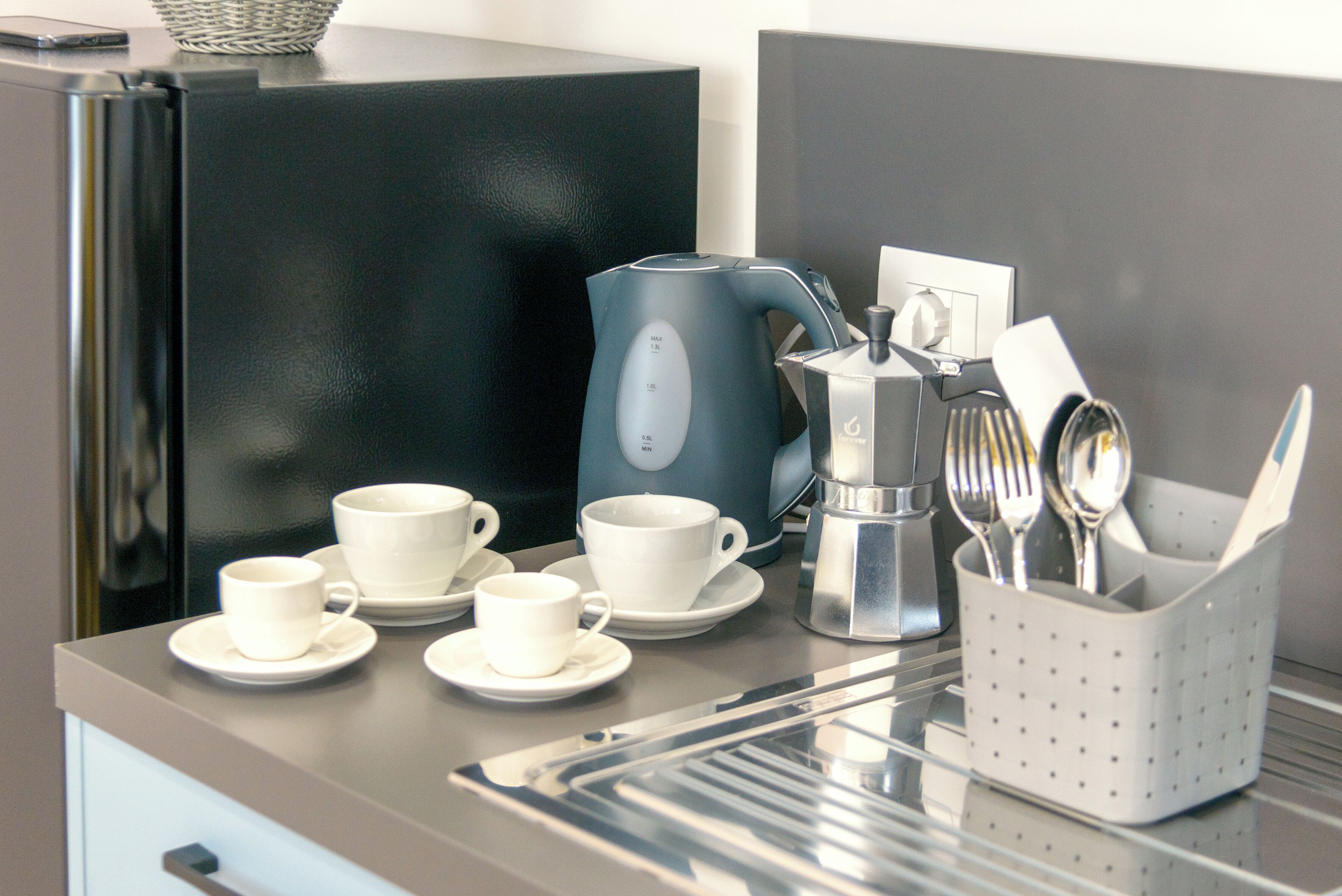 Un espace cuisine moderne avec une machine à café, des tasses et des ustensiles posés sur un plan de travail.