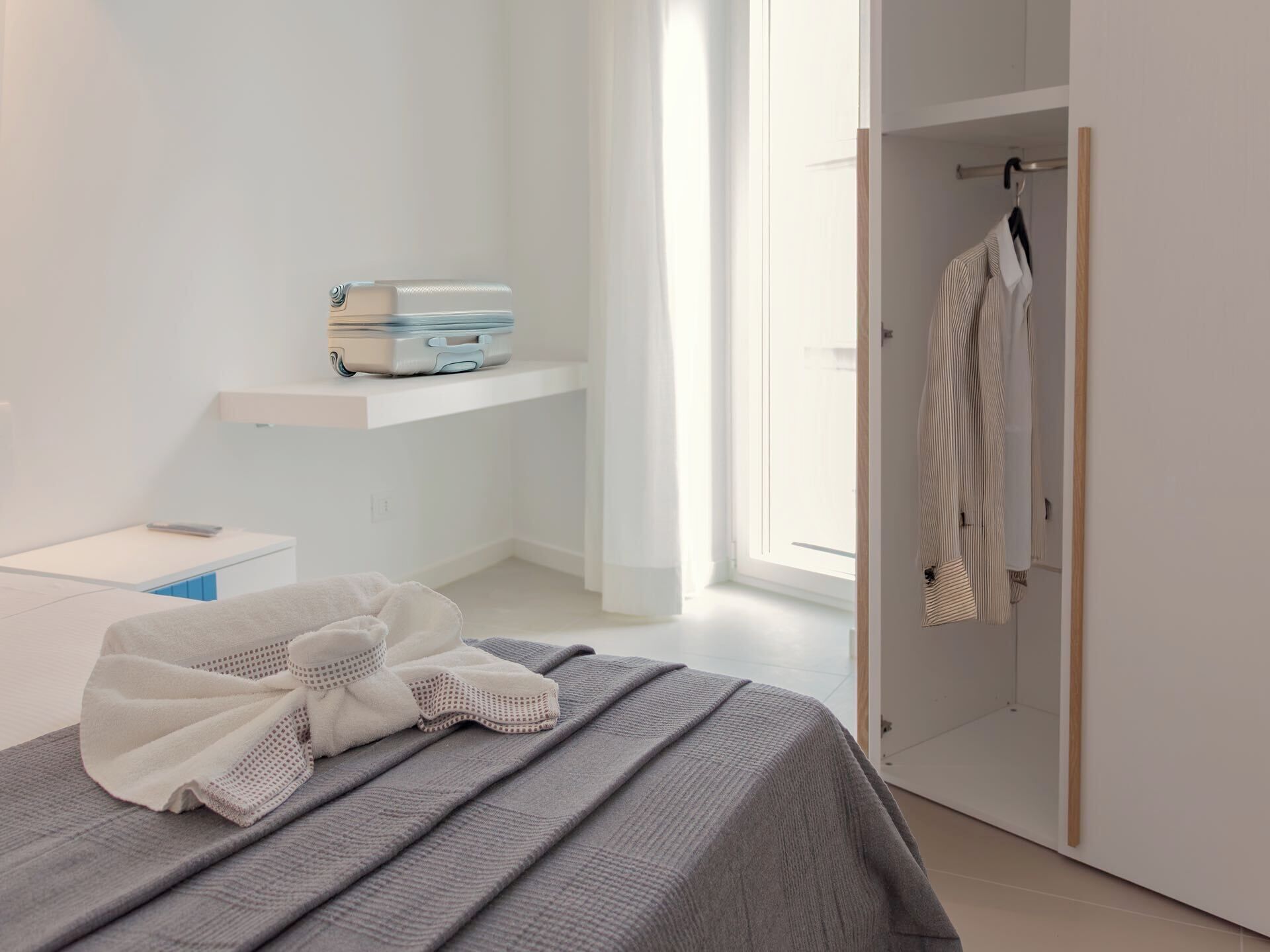 Un dormitorio moderno con cama, mesita de noche, maleta y armario.
