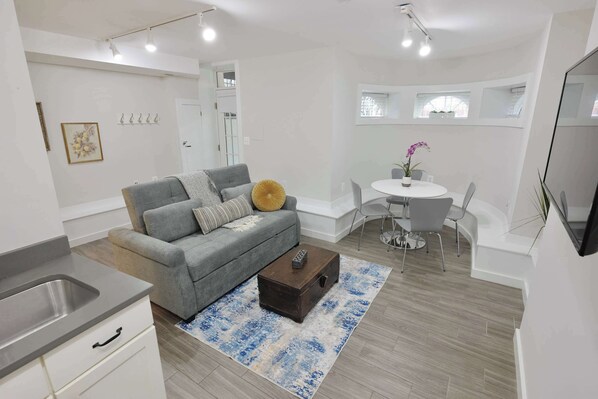 A modern living room with a grey sofa, a coffee table, and a dining area with a white table and chairs.