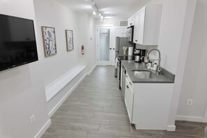 A modern kitchen with white cabinetry, a stainless steel sink, and a flat-screen TV mounted on the wall.