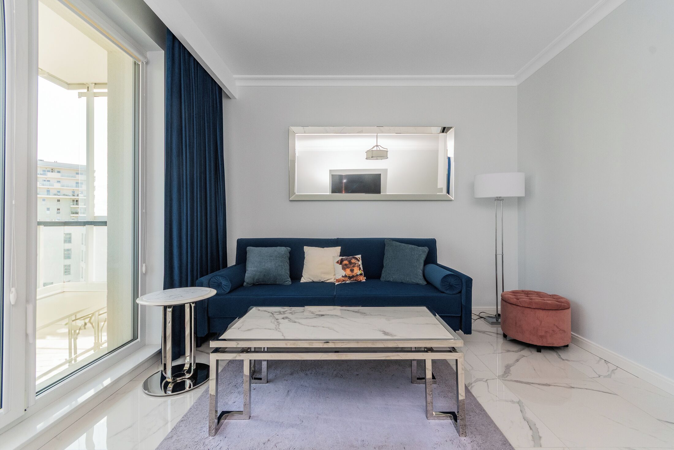 Ein modernes Wohnzimmer mit einem blauen Sofa, einem weißen Couchtisch, einer Stehlampe und einem großen Fenster.