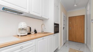 A modern kitchen with white cabinets, a wooden countertop, a coffee maker, a sink, and an oven. - Spektrum 2 by Grand Apartments (Gdansk)