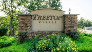 A sign for Treetop Village with a stone wall and flower beds. - Treetop Village Sunset Hollow #105-3BD/3BA/Pools/Grill/Dock/Deck-6PP (Village of Four Seasons)