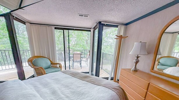 A bedroom with a large bed, a dresser, a chair, and a balcony with a view of trees. - Treetop Village Sunset Hollow #105-3BD/3BA/Pools/Grill/Dock/Deck-6PP (Village of Four Seasons)