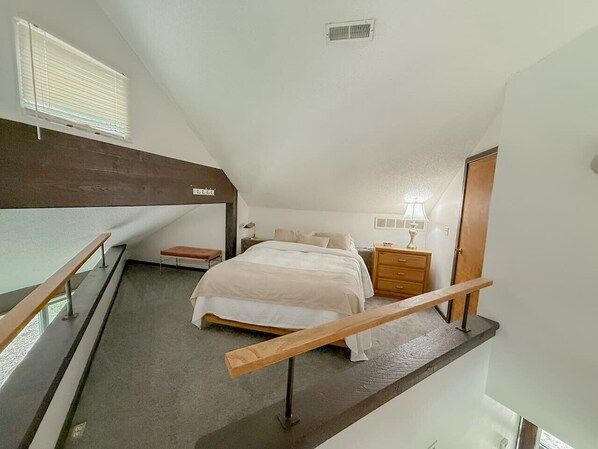 Un dormitorio con cama, mesita de noche, lámpara y ventana con persianas.