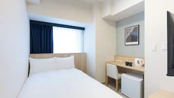 A hotel room with a bed, a desk, a chair, a small refrigerator, and a window with curtains.