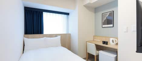 A hotel room with a bed, a desk, a chair, a small refrigerator, and a window with curtains.
