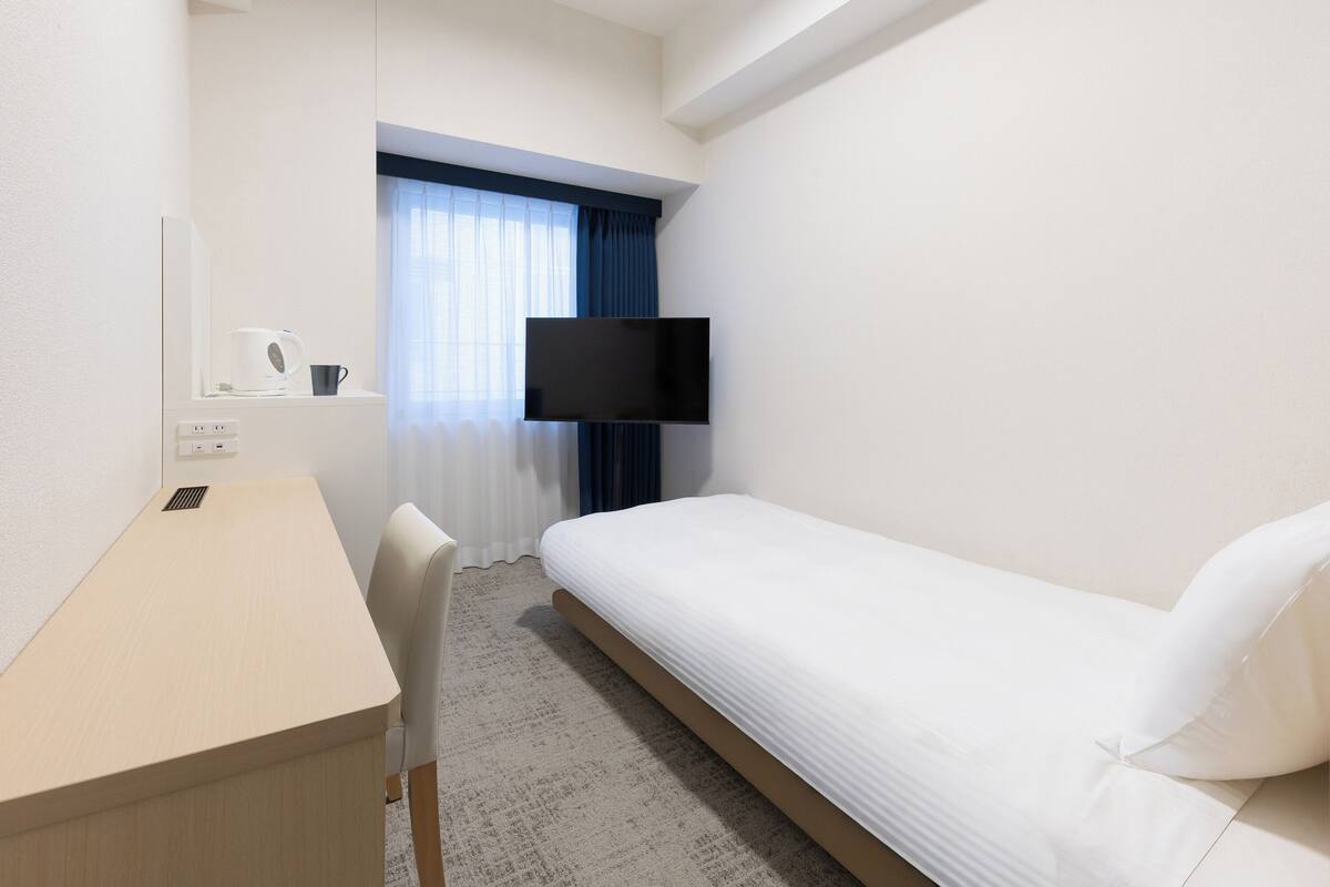 Een hotelkamer met een bed, een bureau, een stoel, een televisie en een raam met gordijnen.
