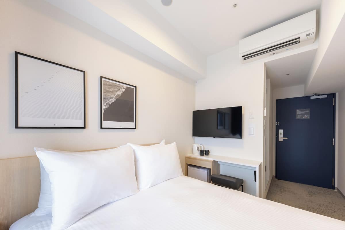 Hotelkamer met een bed, twee ingelijste foto's, een flatscreen televisie, een koffiezetapparaat en een deur.