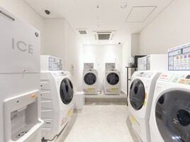 Une laverie équipée de plusieurs machines à laver et de plusieurs séchoirs, y compris des modèles portant les marques « ICE » et « SHARP ».
