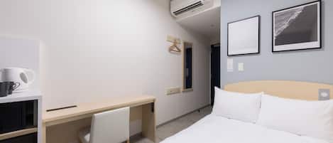 A hotel room with a bed, a desk, a chair, a coffee maker, and an air conditioner.