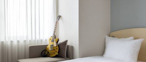 Une chambre d’hôtel avec un lit, une chaise, une guitare et une fenêtre avec des rideaux.