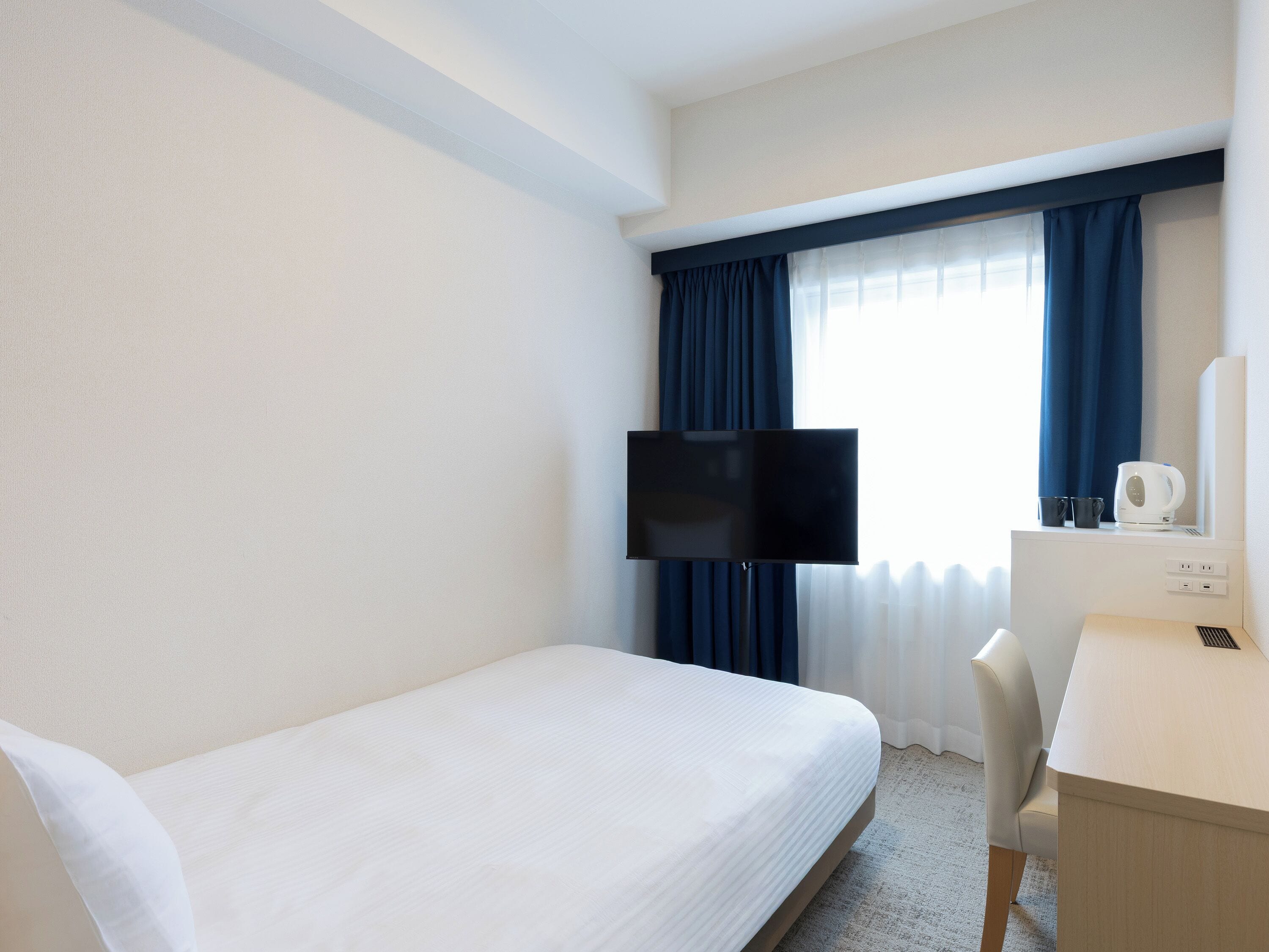 A hotel room with a bed, a desk, a television, and a window with curtains.