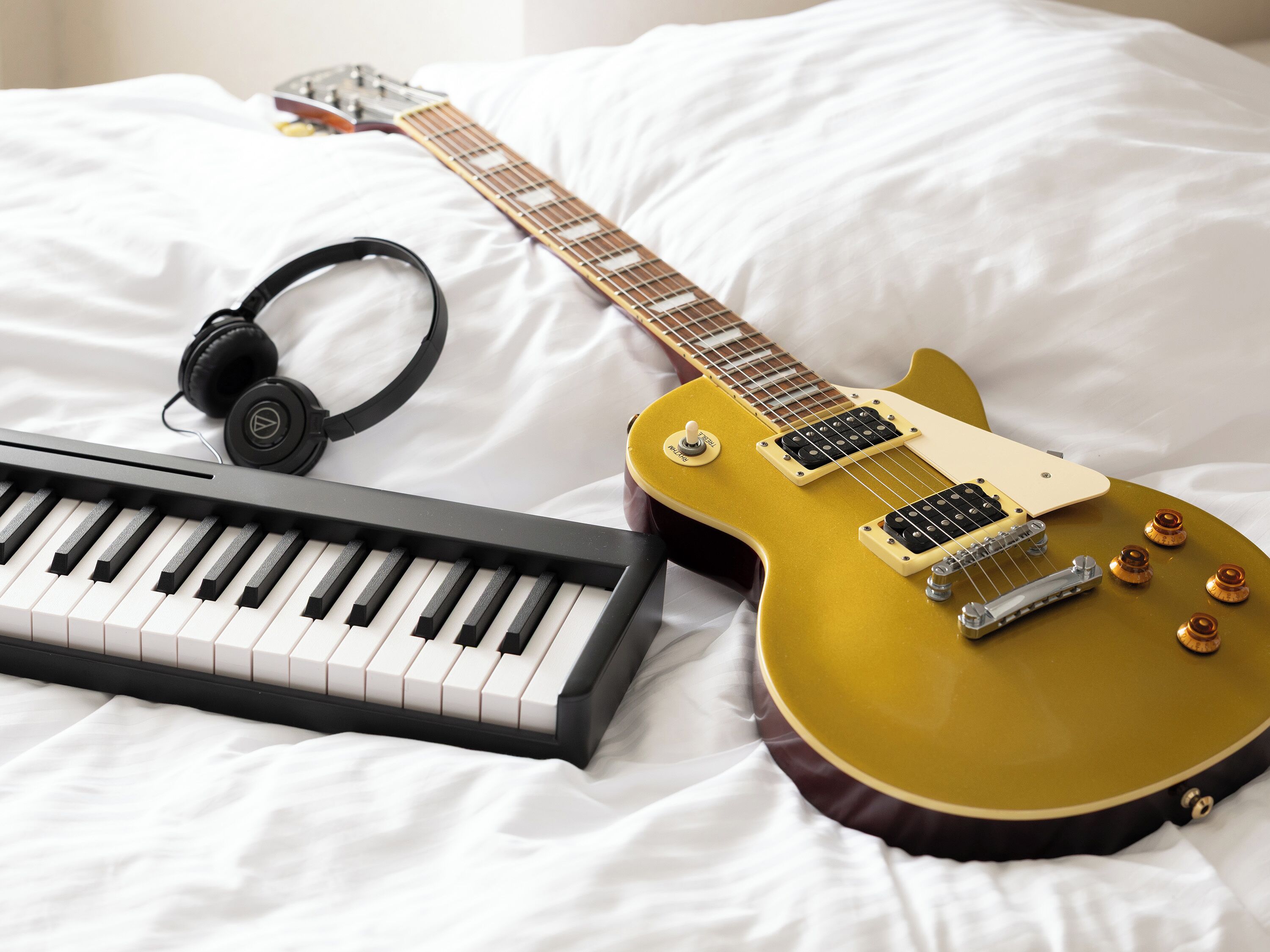 Una cama con una guitarra eléctrica amarilla, un teclado y auriculares.