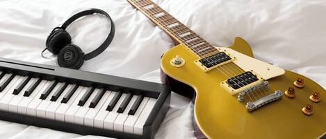 Una cama con una guitarra eléctrica amarilla, un teclado y auriculares.