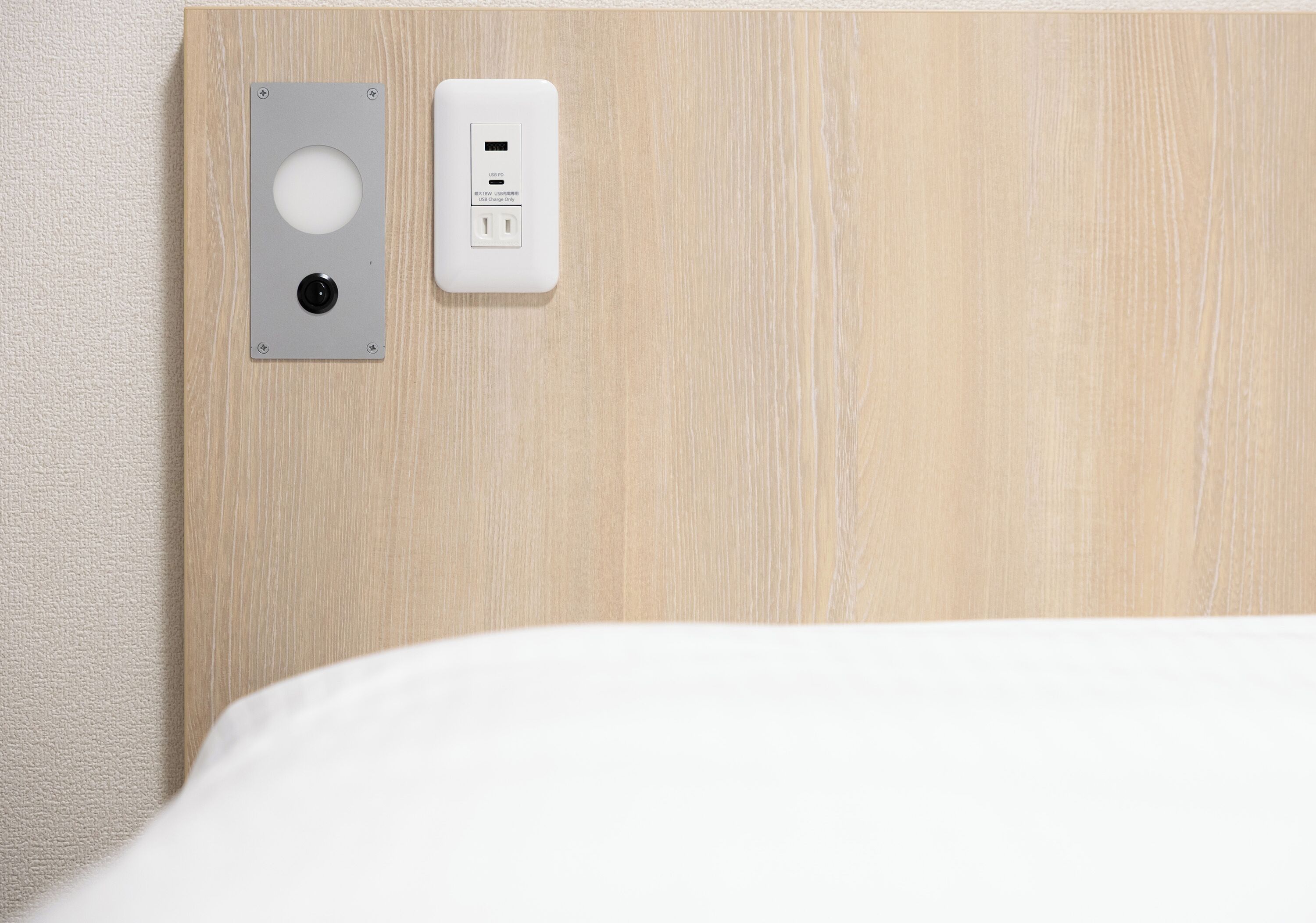 Cabecera de madera con toma de corriente en la pared y una lámpara circular.