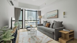 A modern living room with a grey sofa, a round coffee table, a side table, and a large window with curtains. - Marmo by Kozystay - Kuningan (Jakarta)