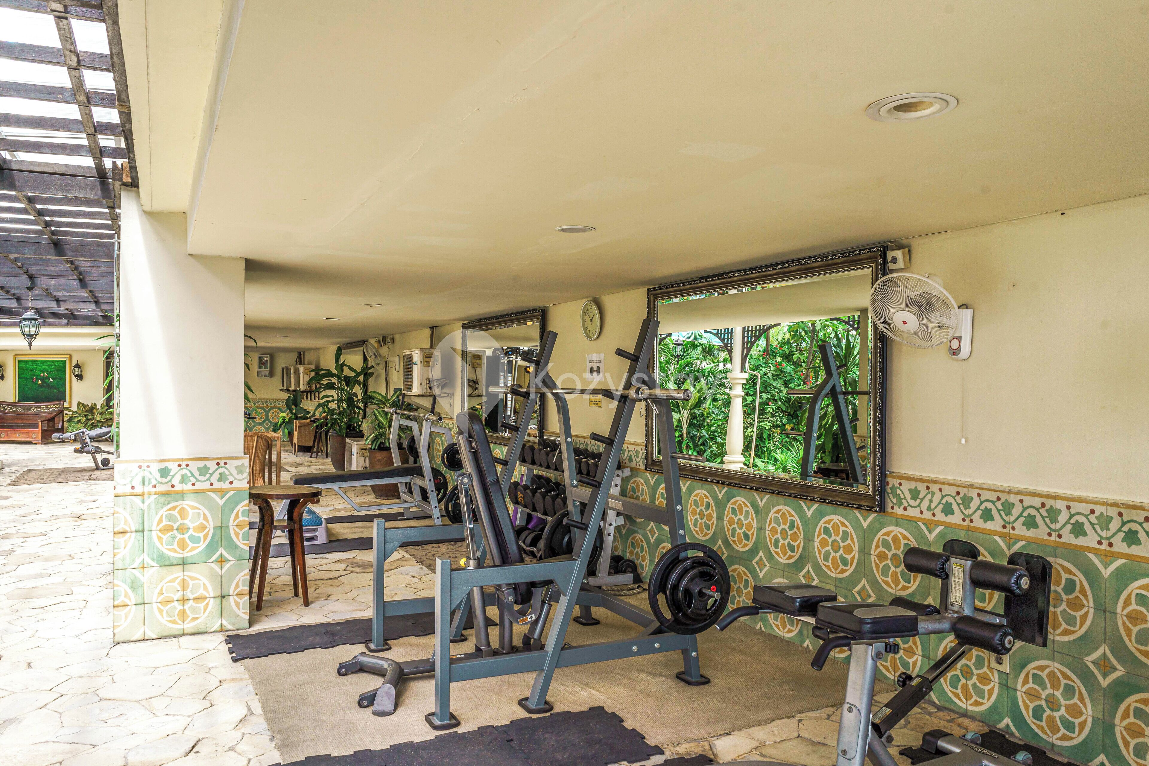 Une salle de sport équipée de matériel d’exercice, avec une horloge et une fenêtre donnant sur un paysage verdoyant.