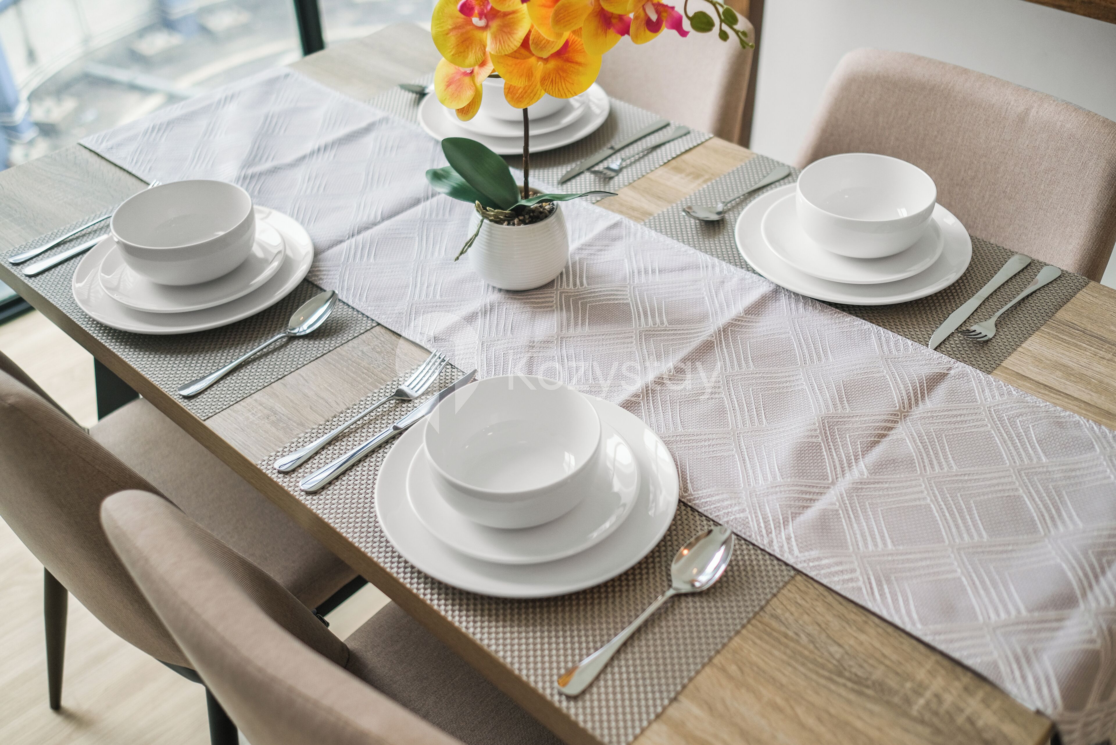 A dining table set with white plates, bowls, and cutlery, with a potted orchid on the table.