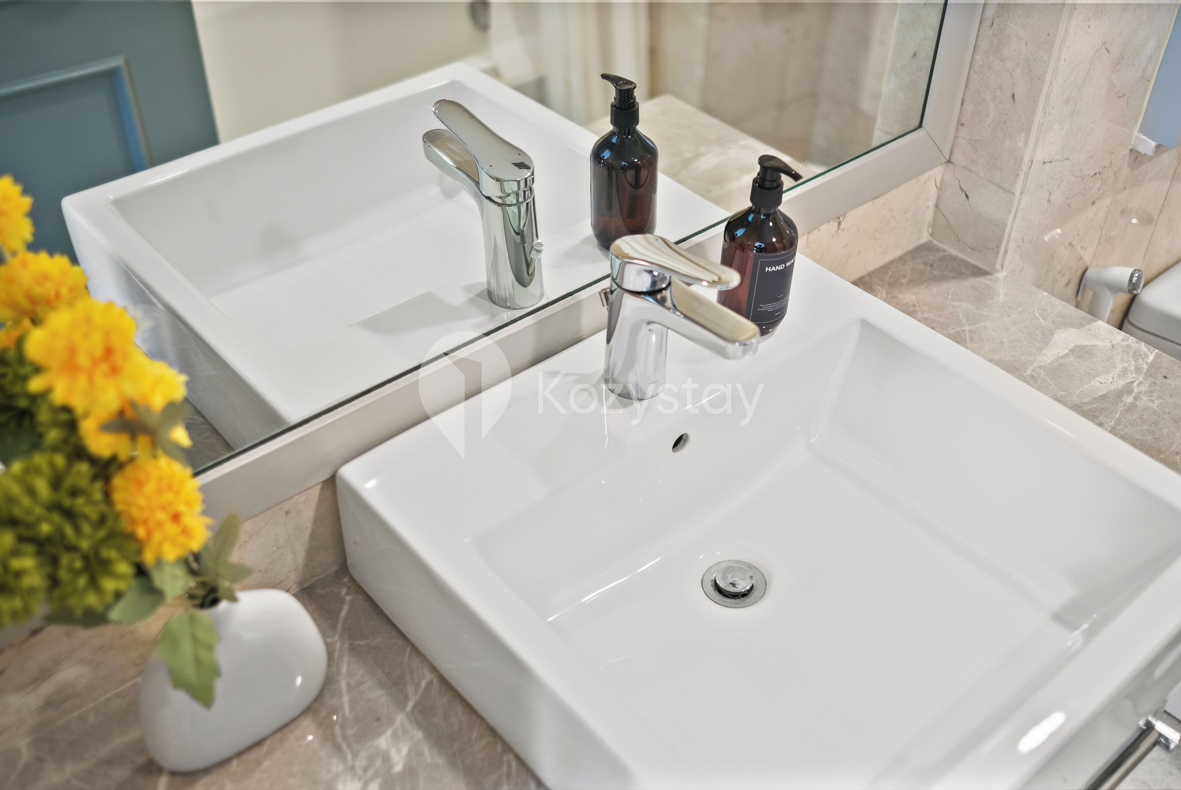Un baño con lavamanos blanco, grifería cromada y un espejo. Hay dos botellas de jabón para manos sobre el lavamanos.