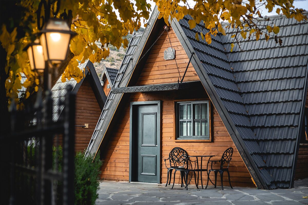 Une cabane en bois avec un toit en pente, une porte et deux chaises à l’extérieur.