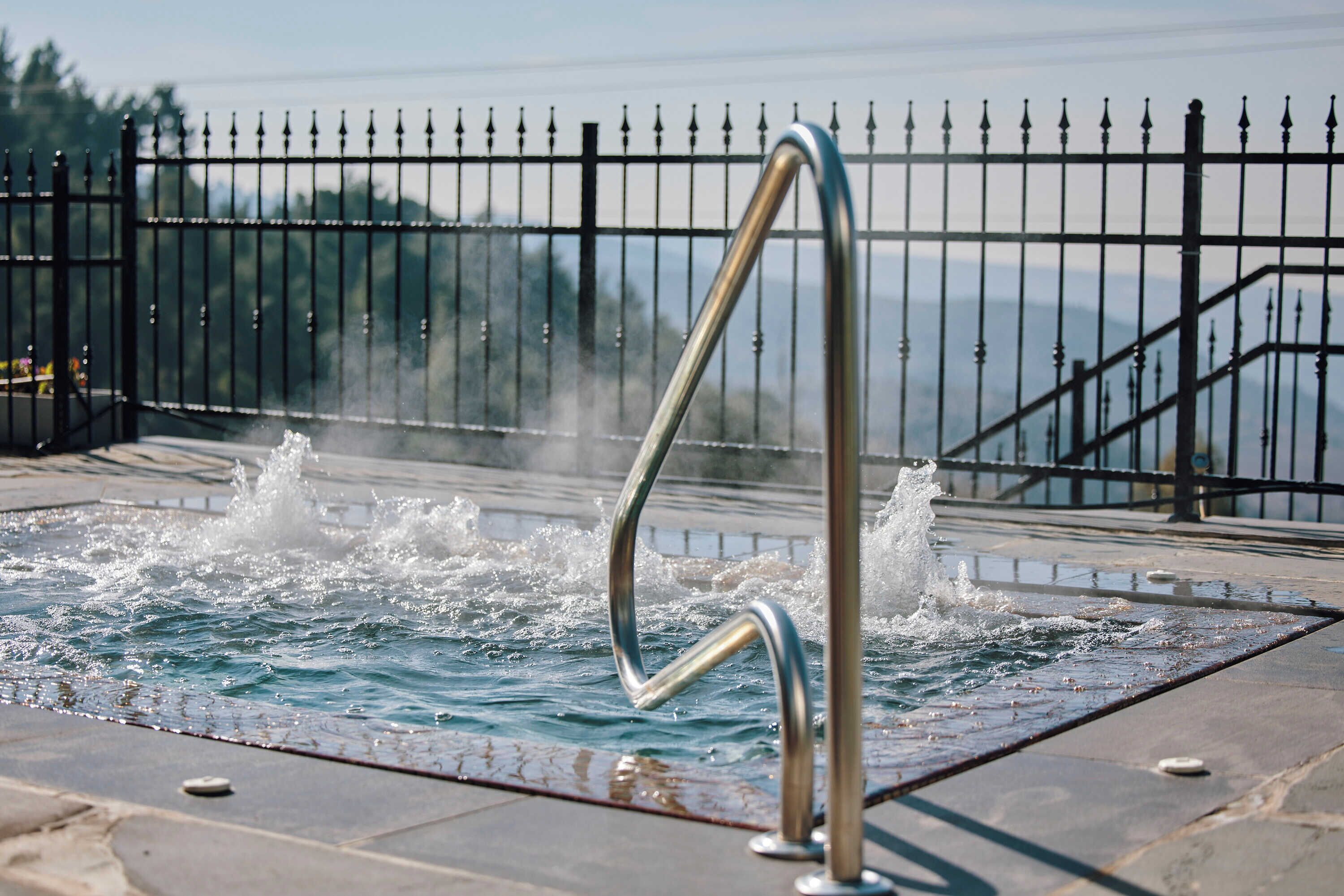 A hot spring with a metal railing, surrounded by a fence and a view of mountains.