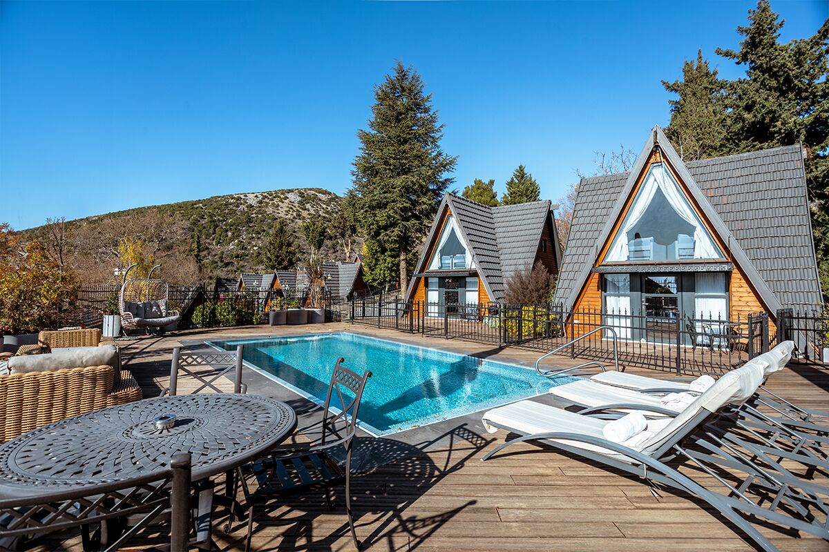 Un área de piscina con sillones de descanso y una mesa, rodeada por una terraza de madera y un paisaje montañoso.