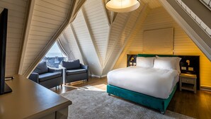 A bedroom with a bed, bedside tables, a desk, and a sofa in a sloped ceiling room.