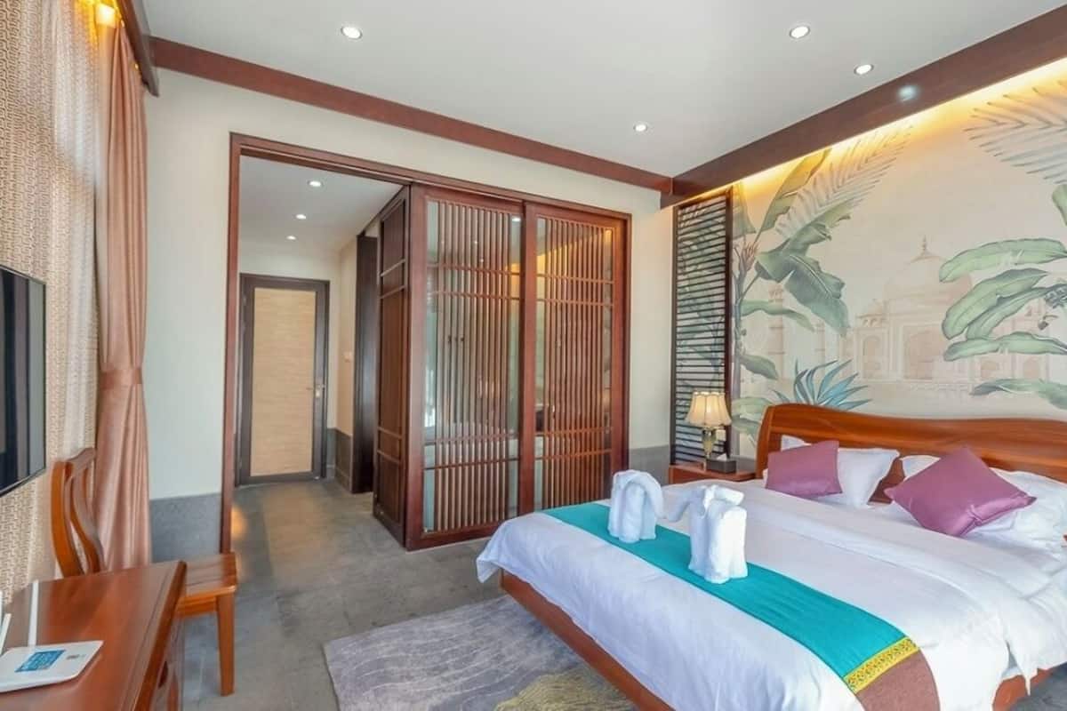 Quarto de hotel com cama, mesas de cabeceira, televisão, escrivaninha e guarda-roupa.