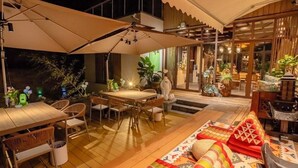 An outdoor dining area with a wooden table and chairs, surrounded by umbrellas and potted plants.