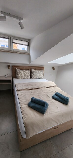A bedroom with a bed, two pillows, a bedside table, a nightstand, a window, and a ceiling light fixture.