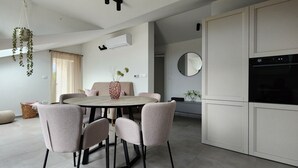 A modern kitchen with white cabinets, a round dining table with six chairs, and hanging plants.