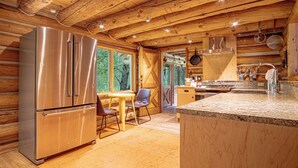 Ein Holzblockhaus-Interieur mit einem Edelstahl-Kühlschrank, einem Esstisch mit Stühlen und einer Küchenzeile mit Spüle und Arbeitsplatte.