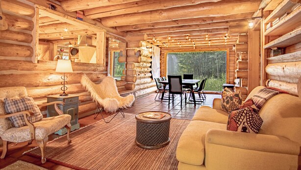 Ein Blockhaus-Interieur mit Essbereich, einer Couch, einem Sessel und einer Lampe.