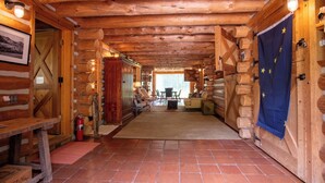 Ein rustikaler Innenraum einer Blockhütte mit Holzbalkendecke, einem Essbereich mit Tisch und Stühlen sowie einem Kamin.