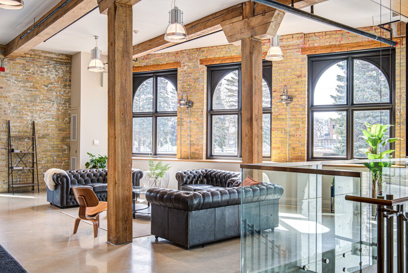 A spacious living area with leather sofas, a wooden ladder, and large windows offering views of trees.