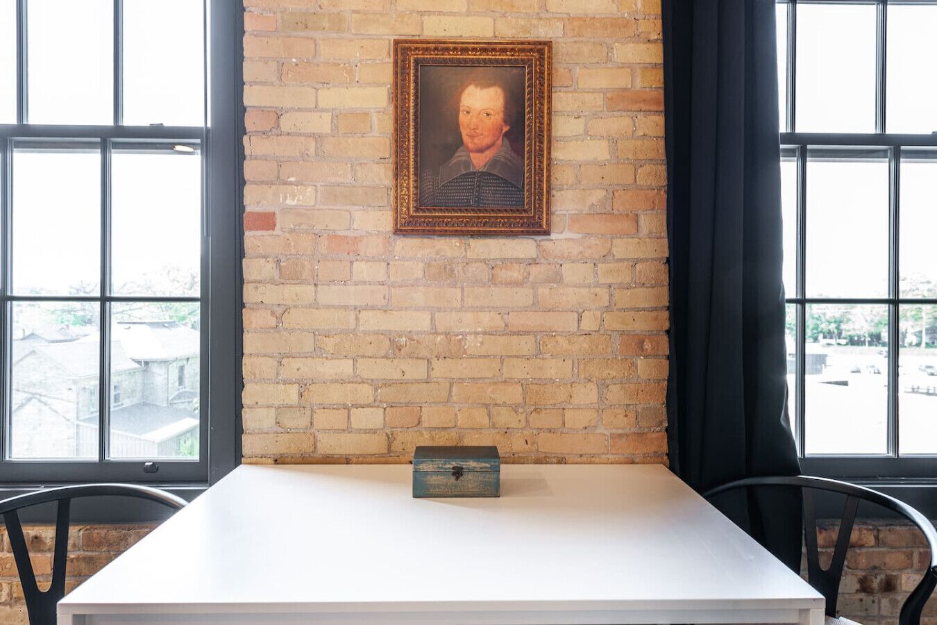 Una habitación con pared de ladrillo, un retrato enmarcado, una mesita y dos sillas.