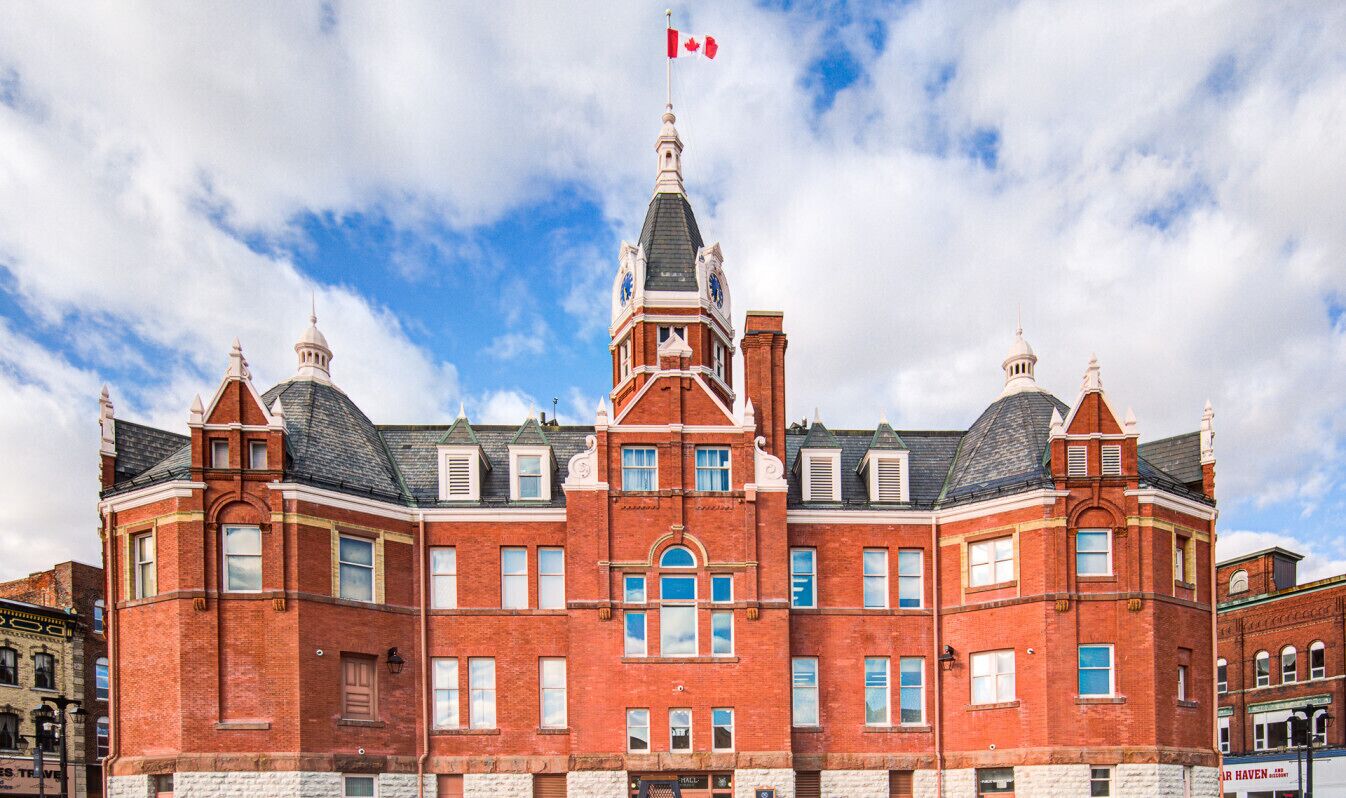 Un edificio grande y antiguo de ladrillo rojo, con una imponente torre del reloj y una bandera canadiense.