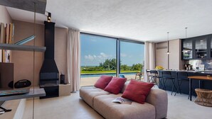 A modern living room with a sofa, a fireplace, and a large window offering a view of the outdoors. - Casa Jems (Noto)
