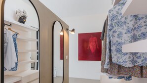 A modern room with a large mirror, a red artwork on the wall, and a white wardrobe with hanging clothes. - Casa Jems (Noto)