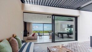 A modern living room with a sofa, a coffee table, and a view of the ocean through large sliding glass doors. - Casa Jems (Noto)