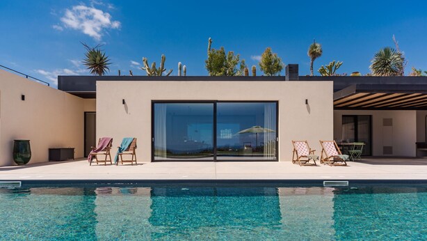 A modern pool area with clear blue water, two lounge chairs, and a view of the sky and desert plants. - Casa Jems (Noto)