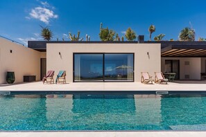 Ein moderner Poolbereich mit klarem, blauem Wasser, zwei Liegestühlen und Blick auf den Himmel und Wüstenpflanzen.