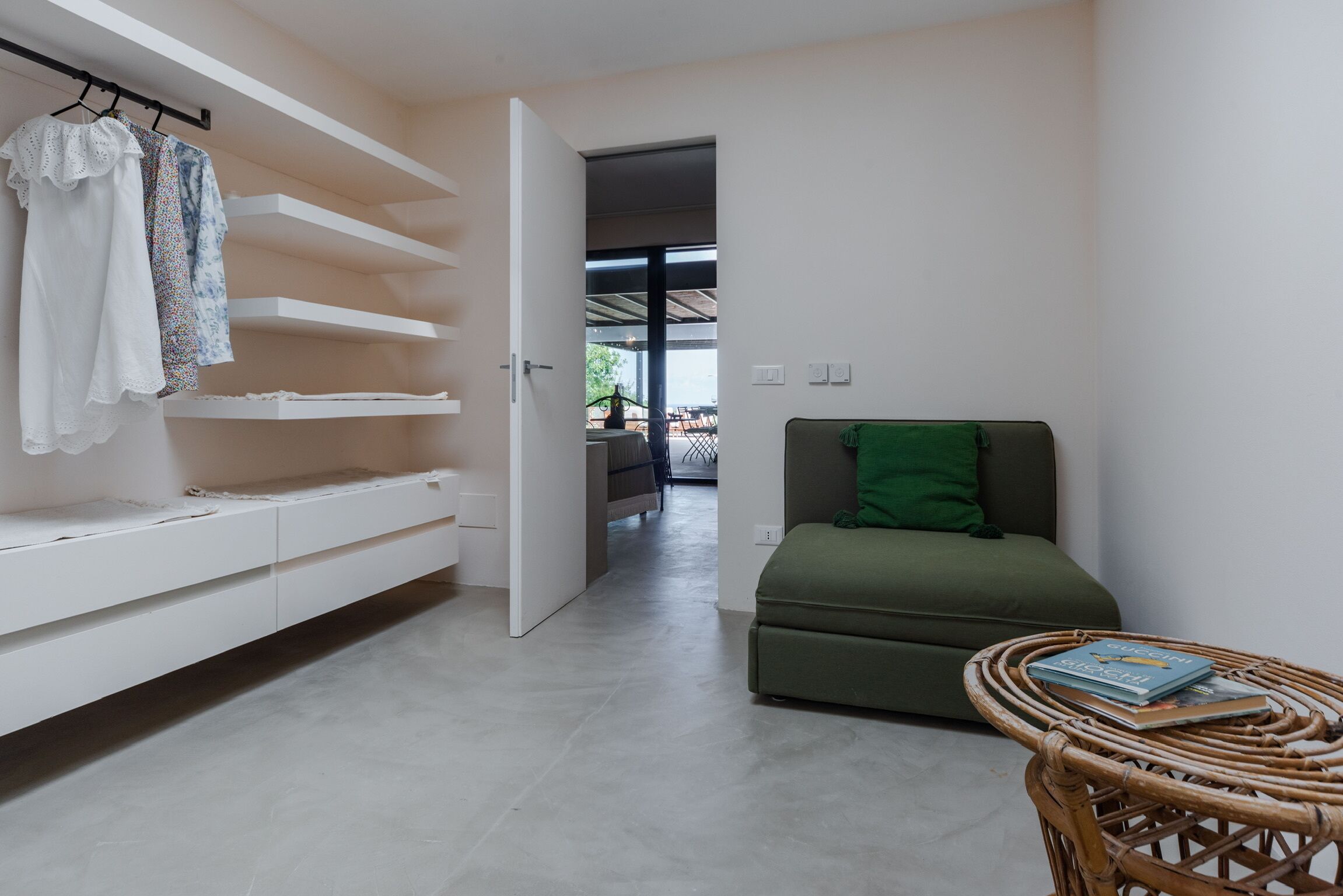 A modern living room with a sofa, a wicker side table with books, and a white built-in shelving unit with hanging clothes.